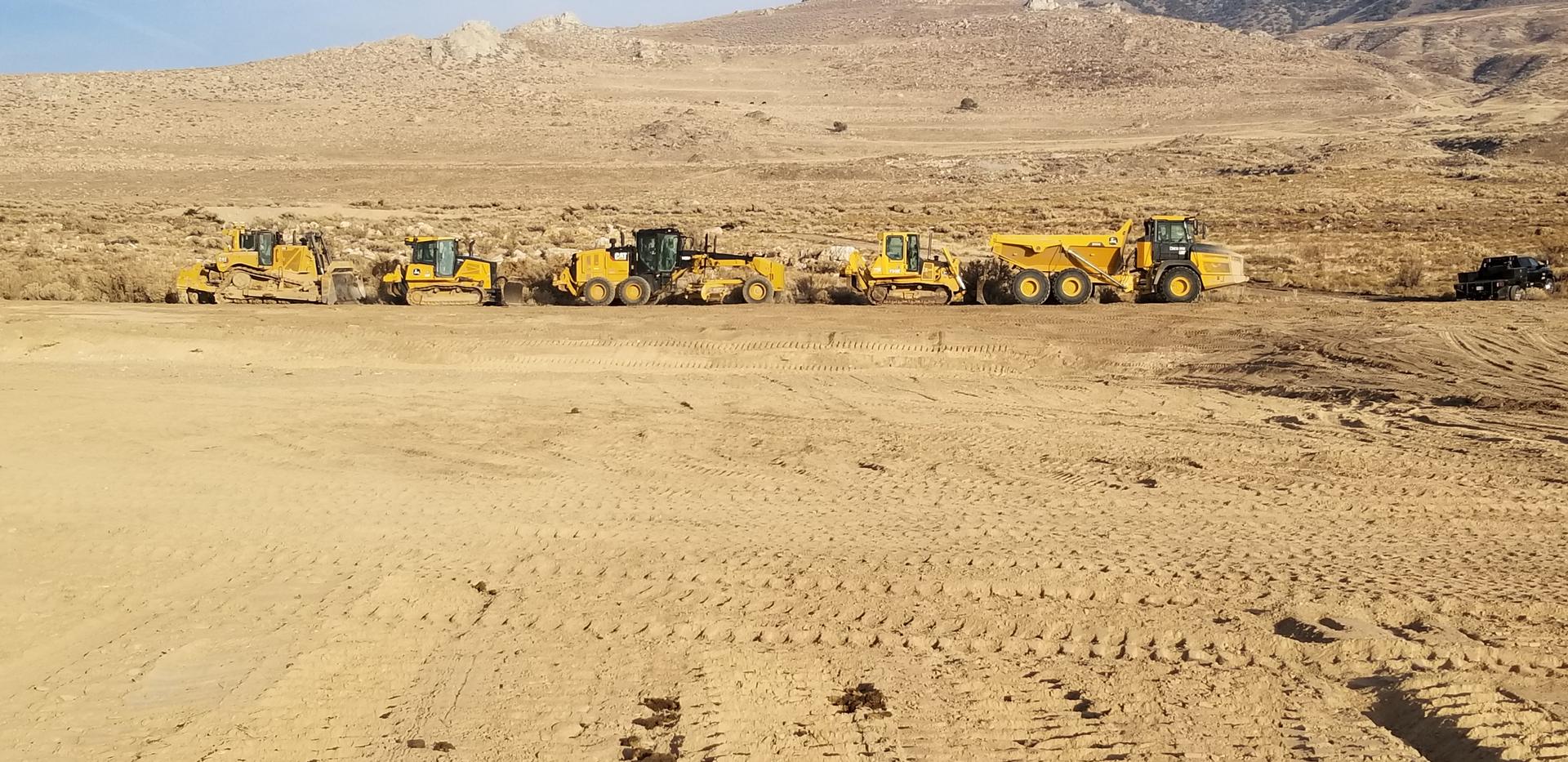Line of excavators, haul trucks, loaders and dozers staged on a large site at dusk