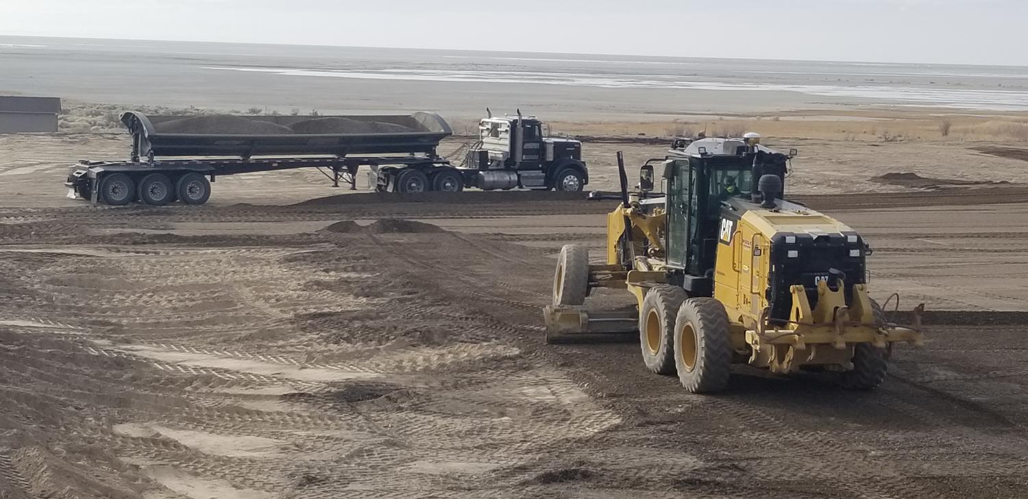 Belly dump trailer delivering base material with a grader spreading it on a large site