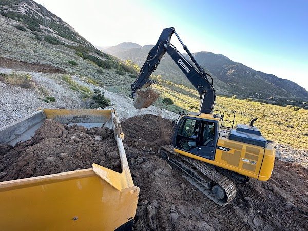 Excavator loading the bed of a haul truck on a hillside cut