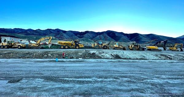 Line of excavators, haul trucks and dozers staged along a subdivision cut at dusk