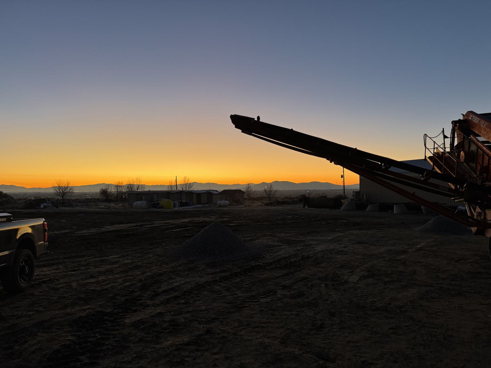 Crushing plant and stacker silhouetted against sunrise on a jobsite, product stockpiled below