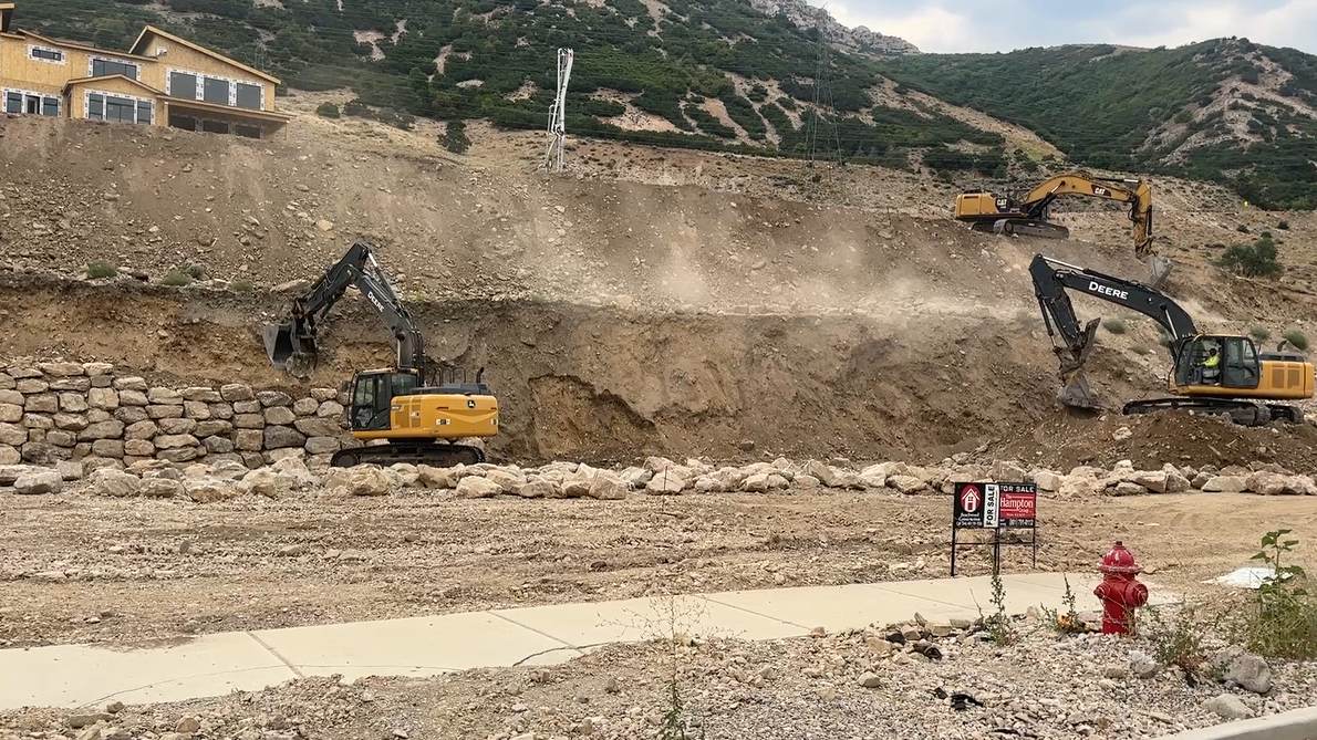 Boulder retaining wall being stacked alongside an active subdivision cut