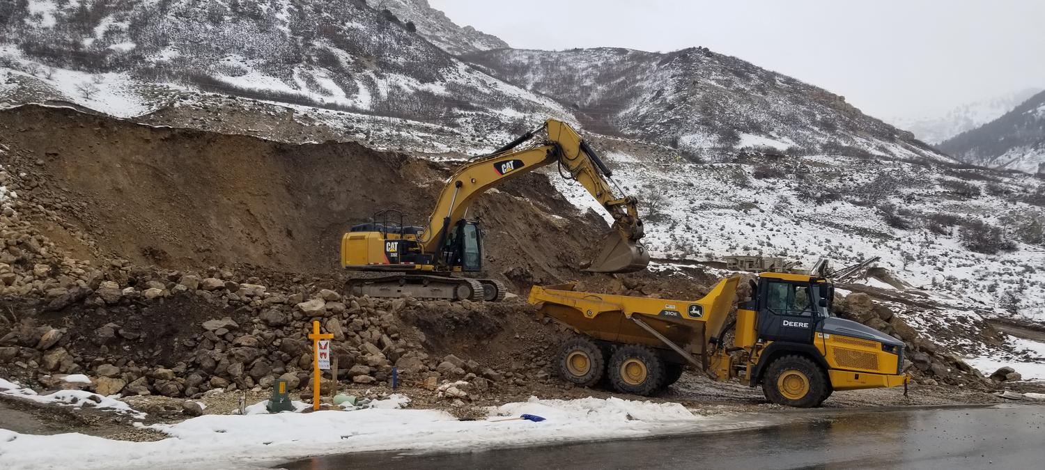 Excavator loading rock into an articulated haul truck on a snow-covered mountainside cut